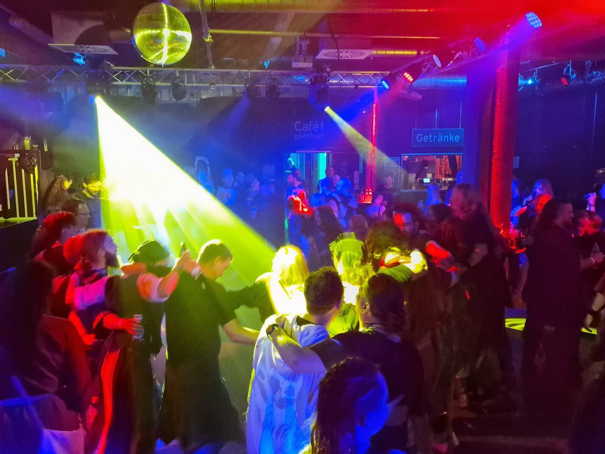 Eine lebhafte Tanzfläche mit bunten Lichtern und feiernden Menschen.