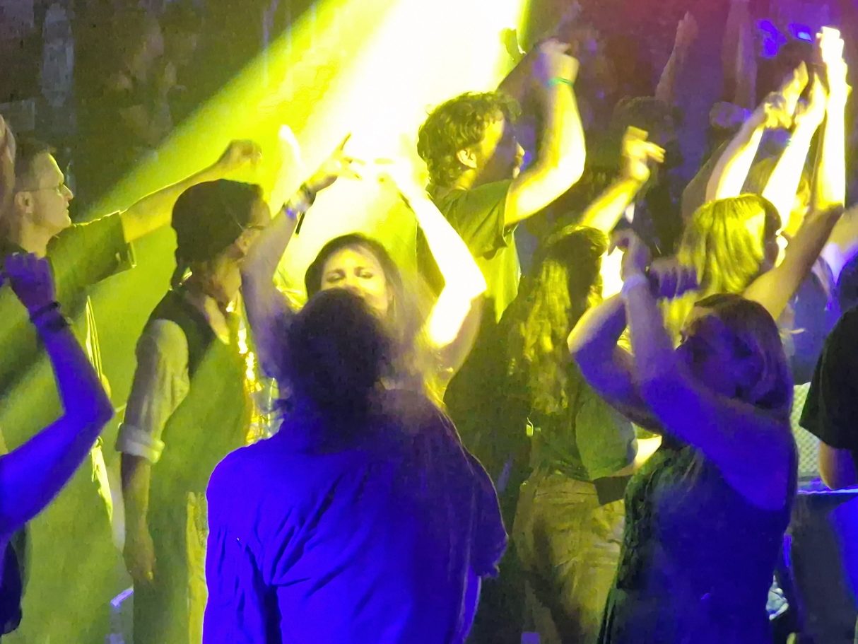 Menschen tanzen und feiern mit bunten Lichtern und energiegeladener Stimmung.
