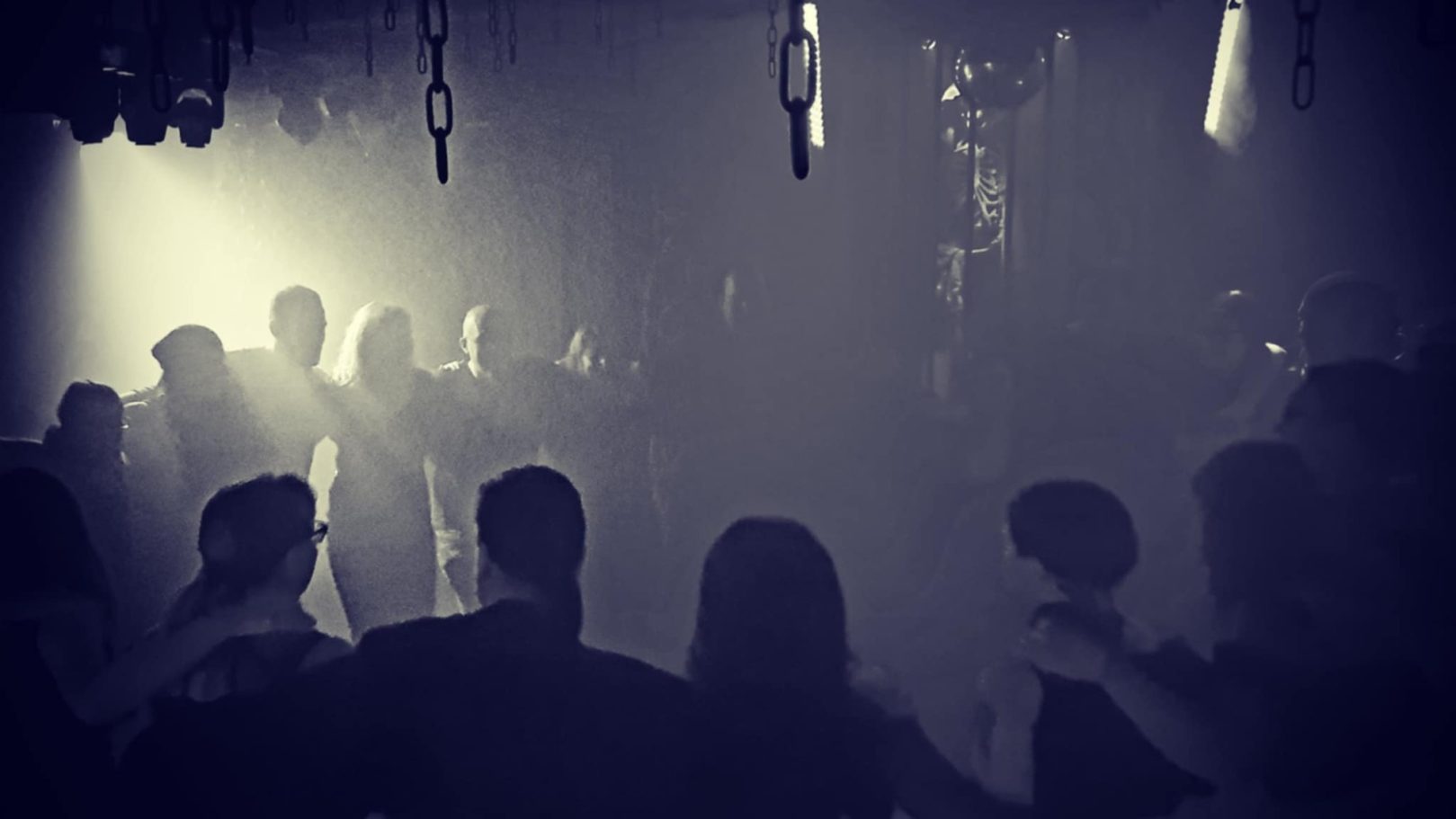 Dunkle Tanzfläche mit Silhouetten von Menschen in einem nebligen Ambiente.